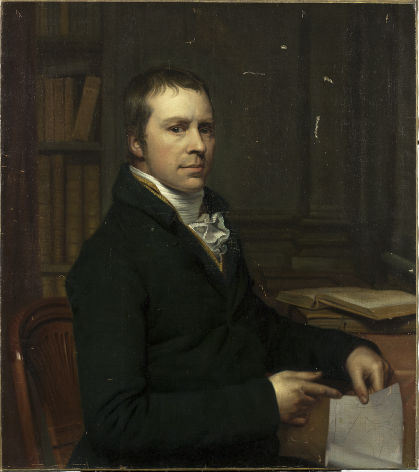 Man aan tafel met papier in de hand, linksachter een boekenkast