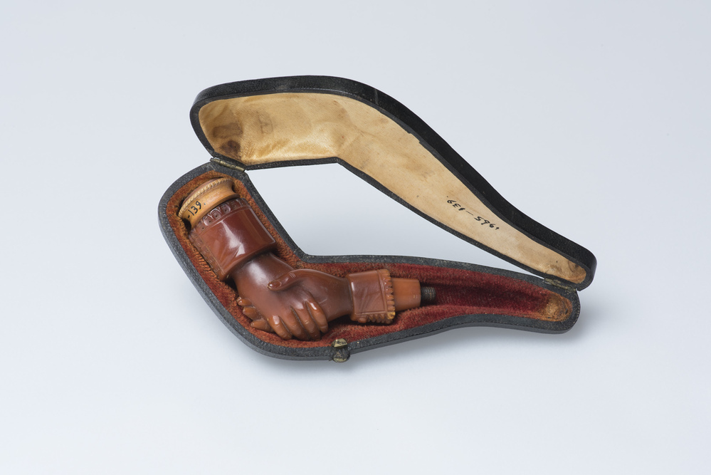 Sigarenpijpje gekroond door twee in elkaar grijpende handen.
In etui